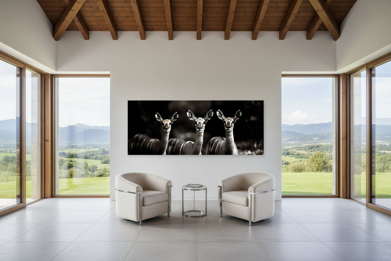 Modern living room with a large wall-mounted artwork of antelopes, surrounded by large windows with a scenic view.